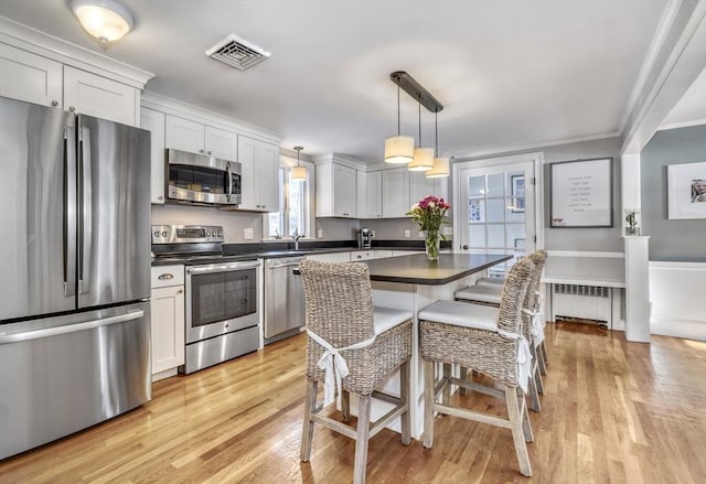 kitchen featuring decorative light fixtures, appliances with stainless steel finishes, a kitchen breakfast bar, radiator, and white cabinets