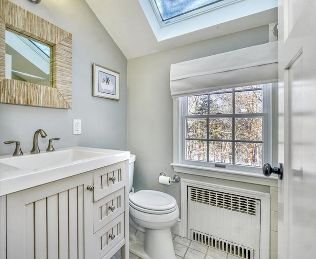 bathroom featuring radiator heating unit, vaulted ceiling with skylight, vanity, tile patterned floors, and toilet