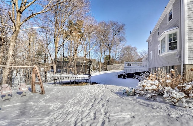 snowy yard featuring a wooden deck and a trampoline