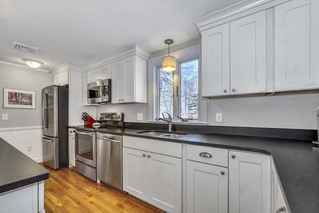 kitchen with appliances with stainless steel finishes, sink, white cabinets, and decorative light fixtures