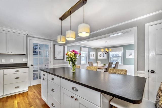 kitchen with decorative light fixtures, ornamental molding, white cabinets, and a kitchen bar