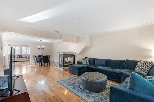 living room with a multi sided fireplace, light wood-type flooring, an inviting chandelier, and ornamental molding