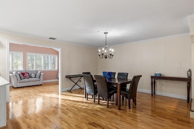 dining space with light hardwood / wood-style floors, an inviting chandelier, and ornamental molding