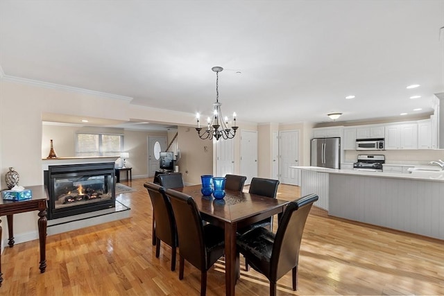 dining room with sink, a multi sided fireplace, light hardwood / wood-style flooring, a chandelier, and ornamental molding