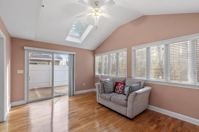 living area with ceiling fan, light hardwood / wood-style flooring, a healthy amount of sunlight, and lofted ceiling with skylight