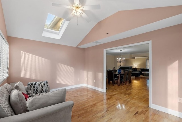 sitting room with hardwood / wood-style floors, ceiling fan with notable chandelier, and lofted ceiling with skylight