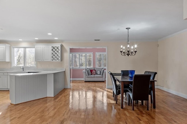 dining area featuring light wood-type flooring, crown molding, and a notable chandelier