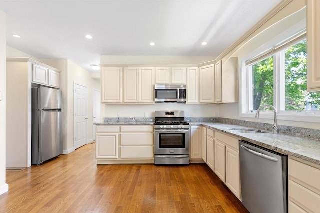 kitchen with light wood-type flooring, recessed lighting, light stone counters, a sink, and appliances with stainless steel finishes