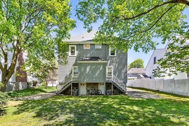 rear view of property with fence, stairs, a lawn, and stone siding