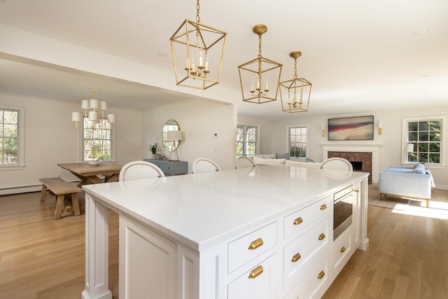 kitchen with an inviting chandelier, light wood-style floors, white cabinetry, stainless steel microwave, and open floor plan