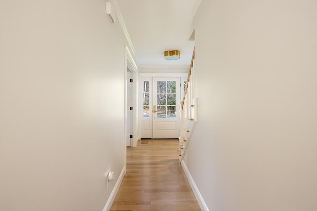 corridor with baseboards, ornamental molding, and light wood-style floors