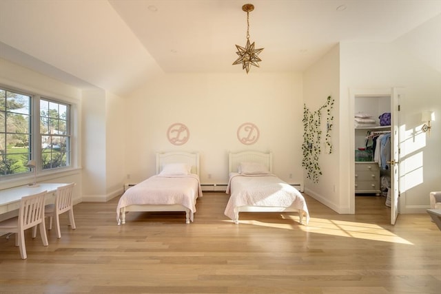 bedroom featuring light wood-style floors, baseboards, a spacious closet, vaulted ceiling, and a baseboard heating unit