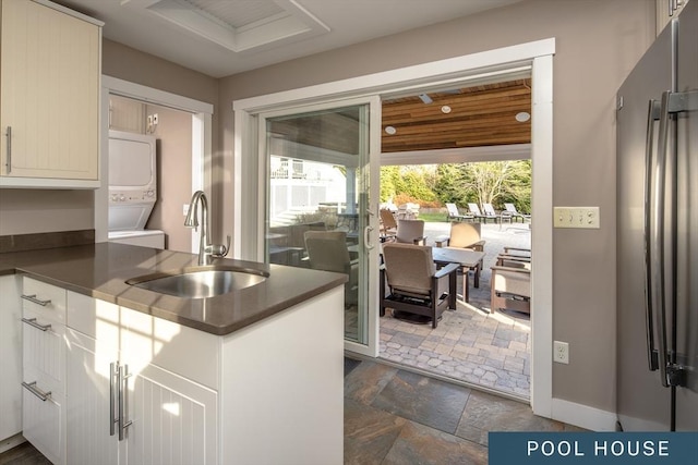 kitchen featuring dark countertops, stacked washer / drying machine, stainless steel fridge, and a sink