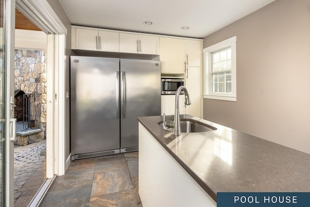 kitchen with stone tile floors, dark countertops, white cabinets, a sink, and appliances with stainless steel finishes