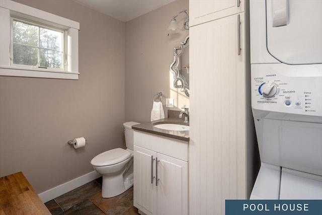 bathroom with stone finish floor, stacked washer / drying machine, vanity, baseboards, and toilet