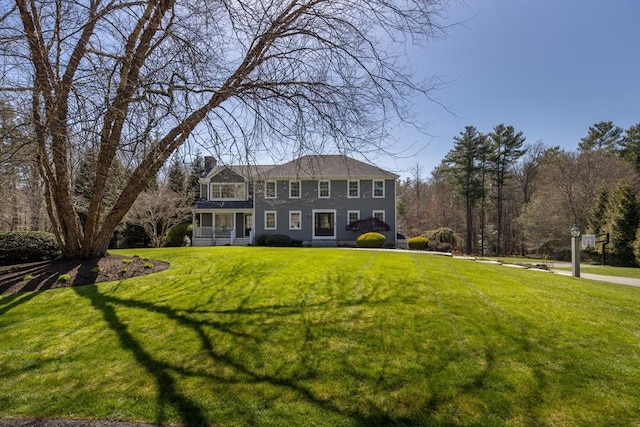 colonial house featuring a front yard, a chimney, and covered porch
