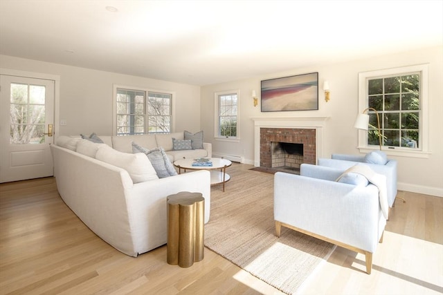 living area featuring a brick fireplace, baseboards, a baseboard heating unit, and light wood-type flooring
