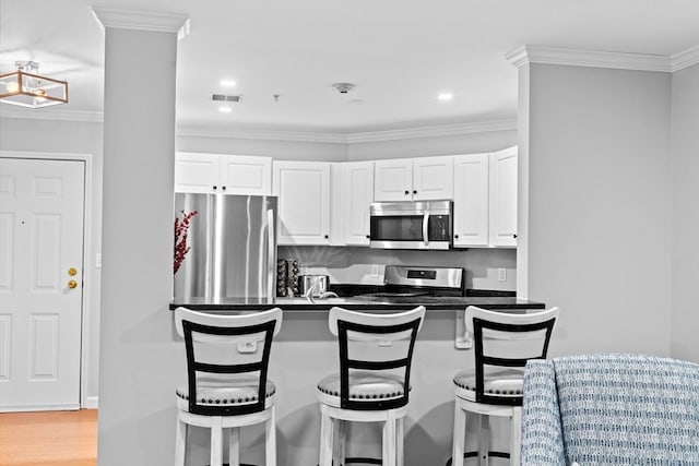 kitchen with appliances with stainless steel finishes, ornamental molding, white cabinets, and a breakfast bar area