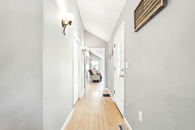 hallway featuring baseboards, vaulted ceiling, visible vents, and light wood-style floors