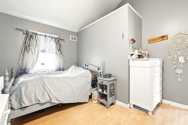 bedroom featuring baseboards, vaulted ceiling, light wood-type flooring, and visible vents