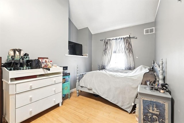 bedroom featuring baseboards, visible vents, light wood-style flooring, and vaulted ceiling