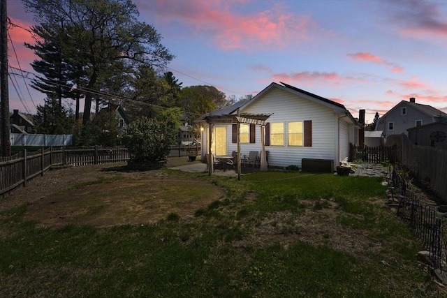 back of property at dusk with a pergola, a fenced backyard, a patio area, and a yard