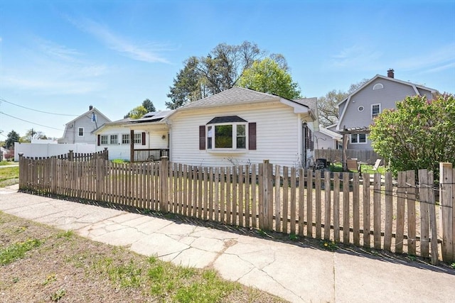bungalow-style home with roof with shingles, fence private yard, and solar panels