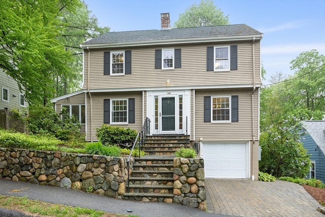colonial inspired home with a chimney, entry steps, a garage, and driveway