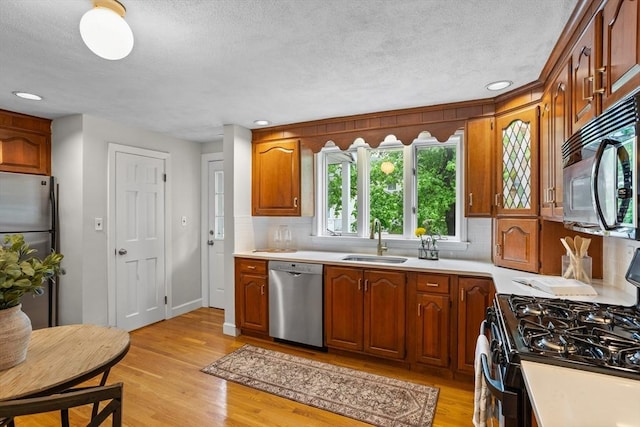 kitchen featuring black appliances, a sink, a textured ceiling, light countertops, and backsplash