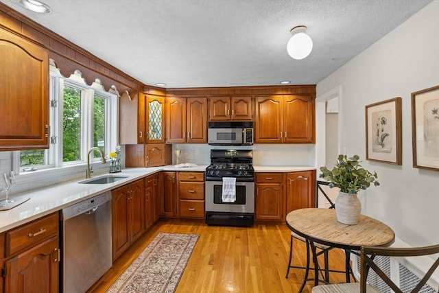 kitchen with stainless steel appliances, a sink, light wood finished floors, light countertops, and brown cabinets