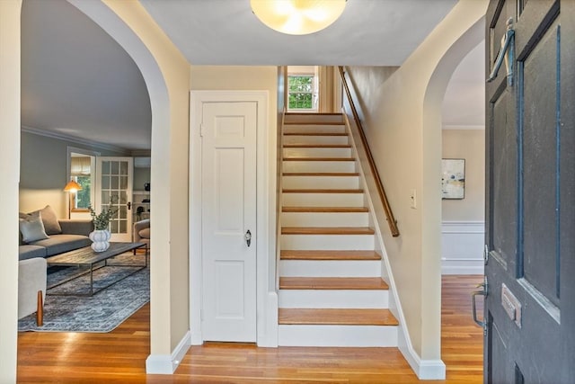 stairway featuring arched walkways, wood finished floors, ornamental molding, and baseboards