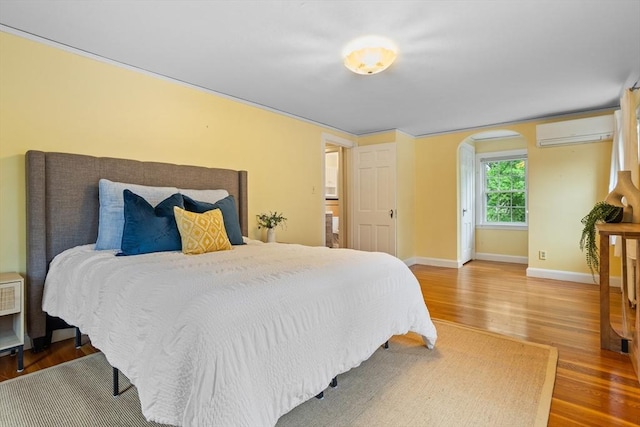 bedroom with an AC wall unit, arched walkways, wood finished floors, and baseboards