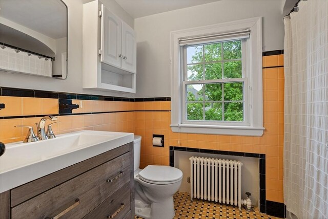 bathroom with radiator, toilet, vanity, tile walls, and a wainscoted wall