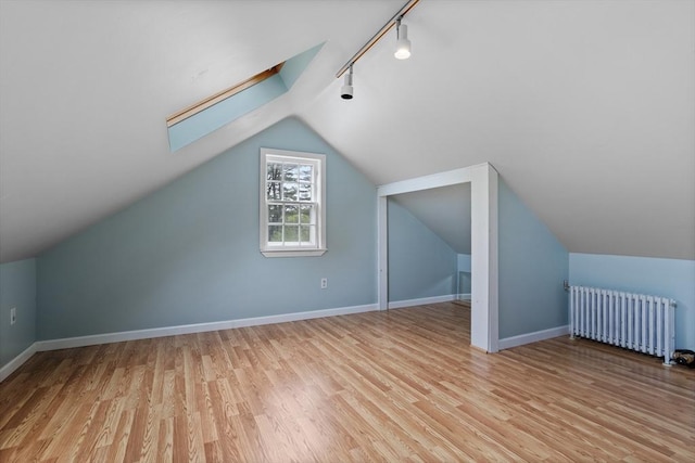 additional living space featuring radiator, light wood-style floors, lofted ceiling, baseboards, and a skylight