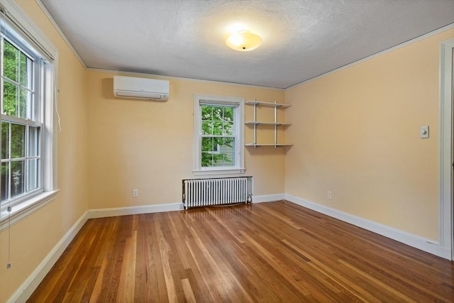 empty room featuring radiator, a wall mounted AC, wood finished floors, plenty of natural light, and a textured ceiling