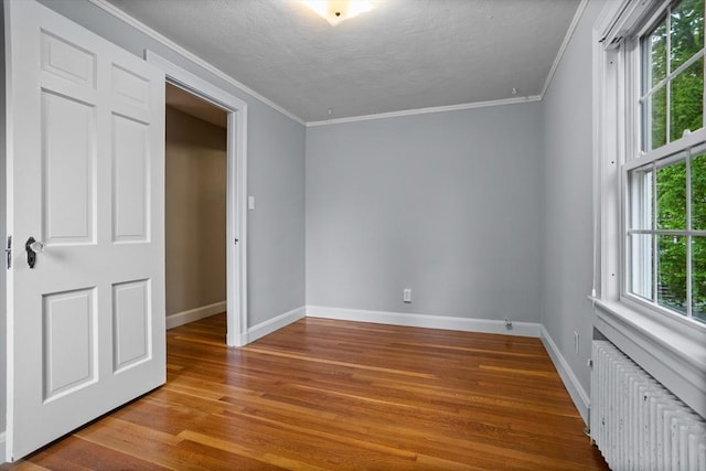 unfurnished bedroom featuring ornamental molding, radiator, wood finished floors, baseboards, and a textured ceiling
