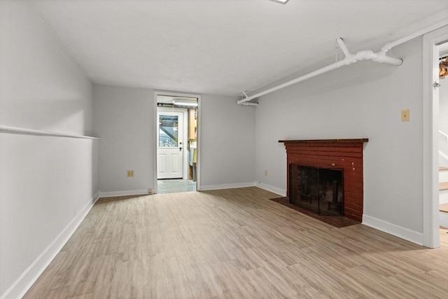 unfurnished living room with light wood-type flooring, a brick fireplace, and baseboards