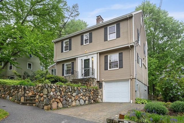 colonial inspired home featuring decorative driveway, a garage, and a chimney
