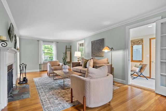 living area featuring light wood-type flooring, crown molding, radiator heating unit, a fireplace with flush hearth, and baseboards