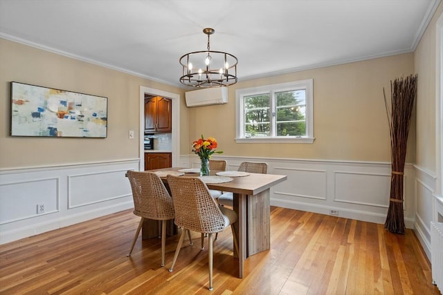 dining room featuring a wall unit AC, a chandelier, crown molding, light wood-style flooring, and a decorative wall
