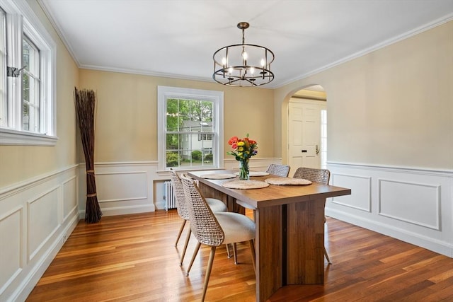 dining space featuring arched walkways, ornamental molding, light wood-style floors, a chandelier, and wainscoting