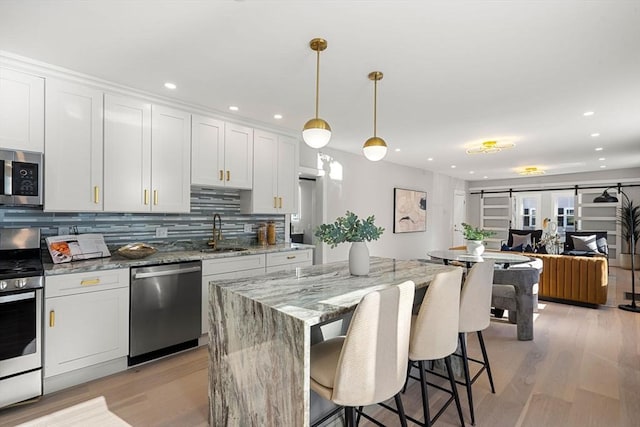 kitchen featuring stainless steel appliances, a barn door, white cabinets, and decorative light fixtures