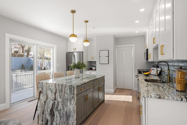 kitchen with appliances with stainless steel finishes, a kitchen island, white cabinetry, hanging light fixtures, and light stone countertops