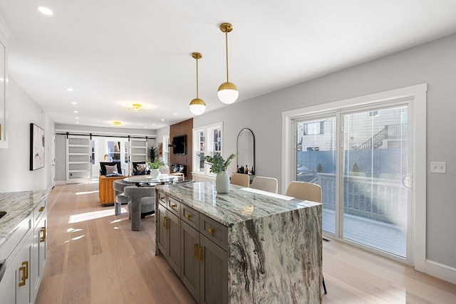 kitchen with light stone counters, hanging light fixtures, a barn door, and light wood-type flooring