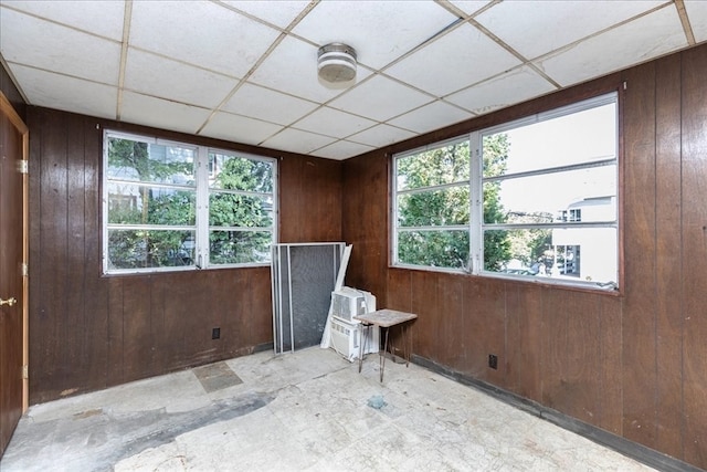 empty room featuring a drop ceiling, a wealth of natural light, and wood walls