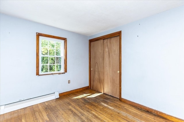 unfurnished bedroom featuring light wood-type flooring, a closet, and a baseboard heating unit