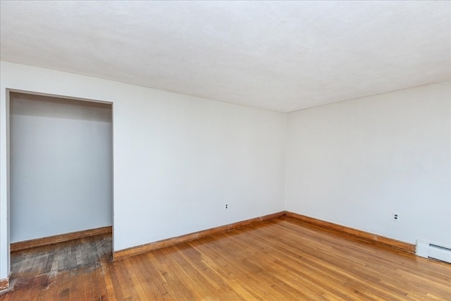 empty room featuring hardwood / wood-style floors and a baseboard heating unit