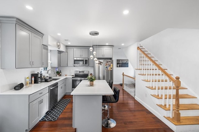 kitchen featuring dark wood-style floors, gray cabinets, appliances with stainless steel finishes, and a kitchen breakfast bar