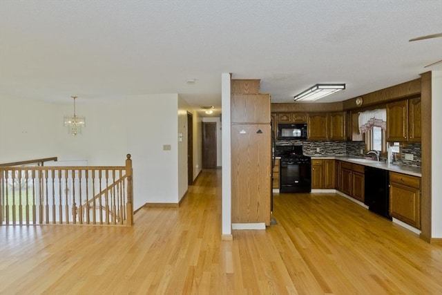 kitchen with brown cabinetry, light wood-type flooring, light countertops, black appliances, and a notable chandelier