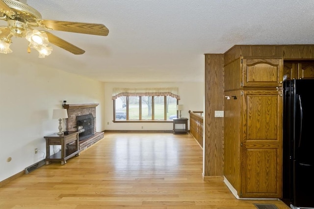 living area featuring visible vents, a ceiling fan, light wood-style flooring, and a fireplace